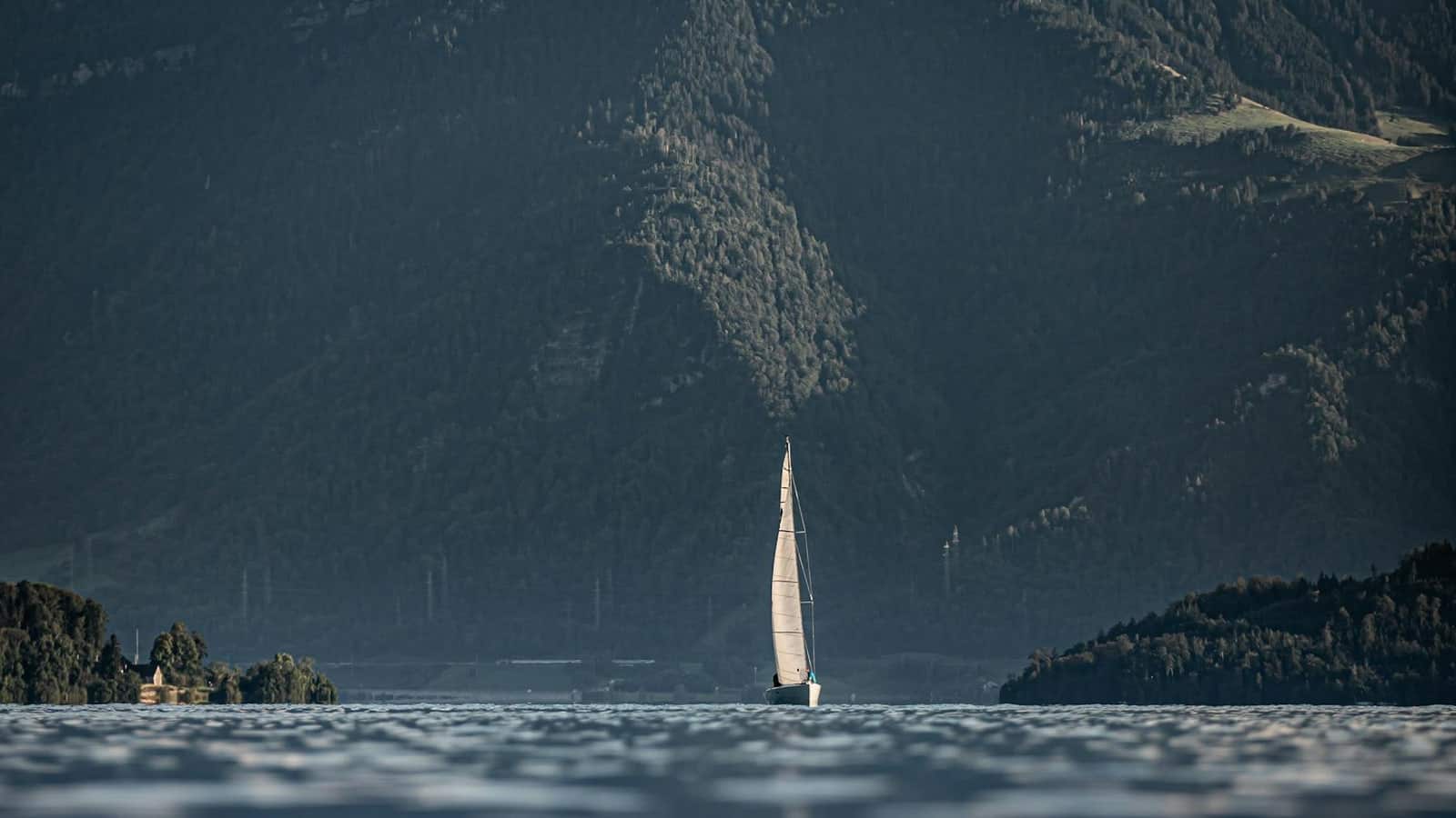 Weisses Segelboot auf dem Zugersee vor dunkler Bergkulisse